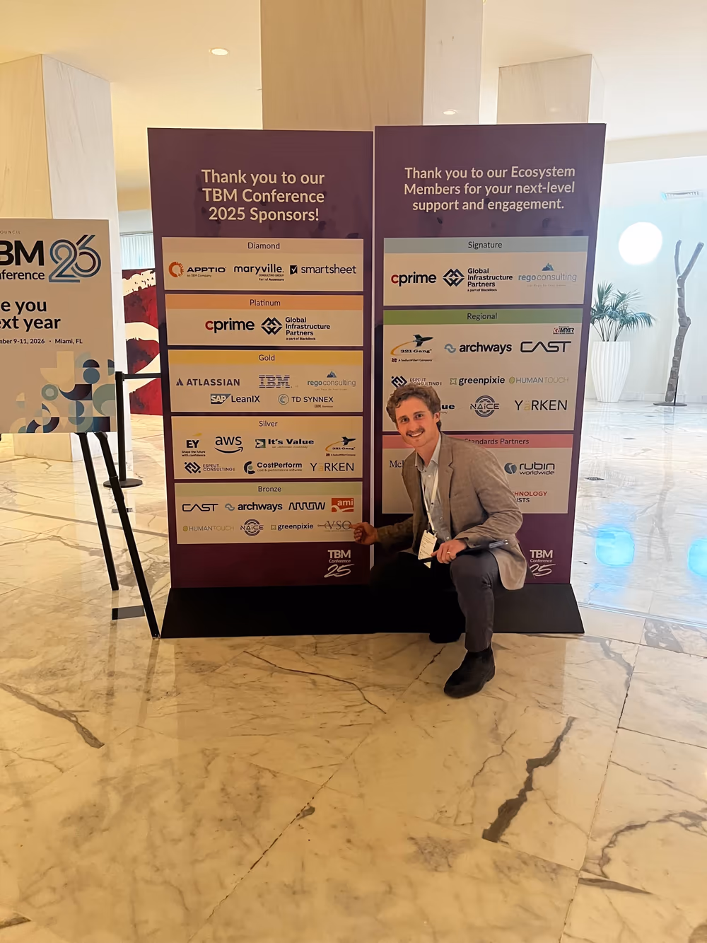 A FogLifter team member pointing to the VSO logo on the TBM Conference 2025 sponsor wall